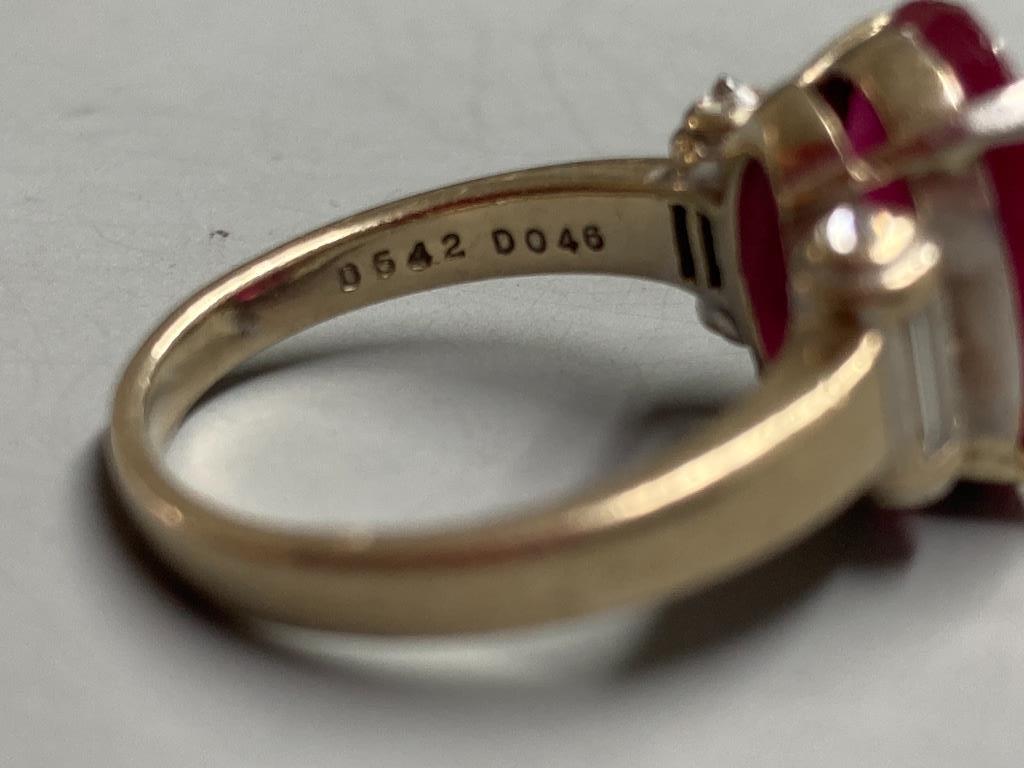 A modern yellow metal (stamped 750) and oval cut single stone ruby dress ring, with baguette cut diamond set shoulders